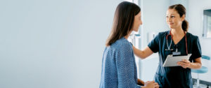 Provider in profile wearing blue scrubs, smiling at patient that is sitting on exam room table
