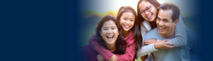 Asian family of four, young daughters hugging parents from behind - smiling outdoors